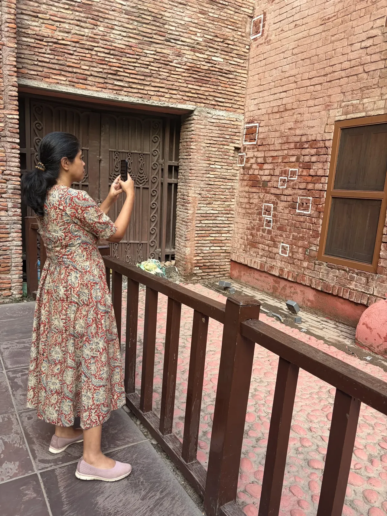 Visitor photographing the bullet-hole marked brick wall at Jallianwala Bagh, Amritsar heritage tour