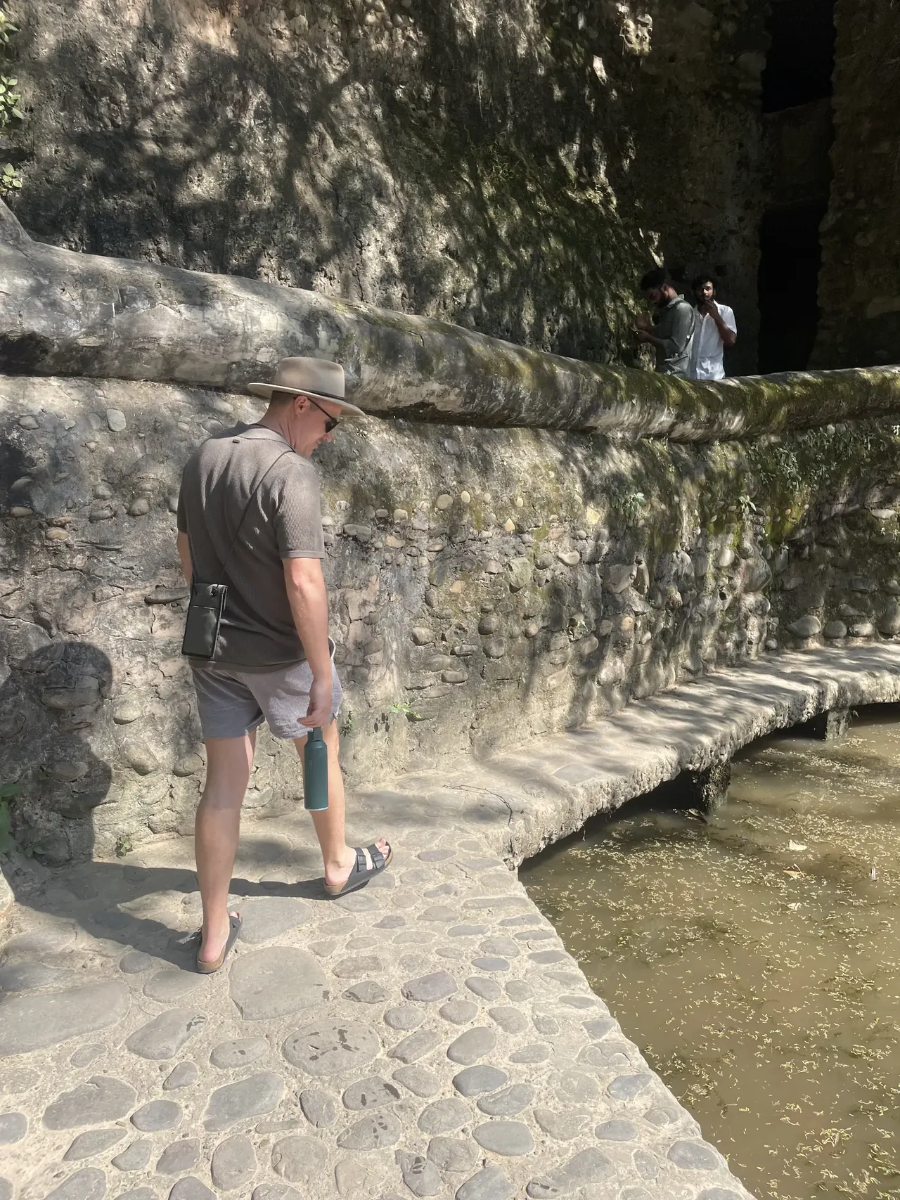 Visitors crossing a stone walkway bridge over water inside the Rock Garden, Chandigarh architecture tour